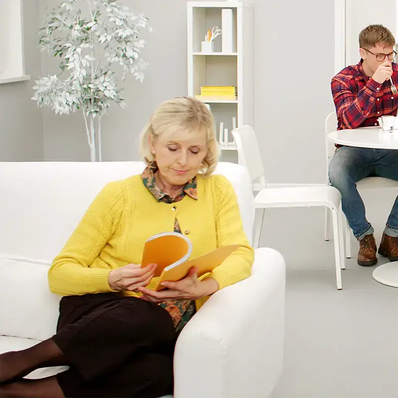 En person i gul kofta sitter i en vit soffa och l&auml;ser en bok